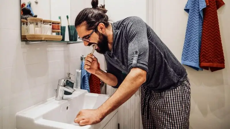 A man brushes his teeth at a bathroom sink