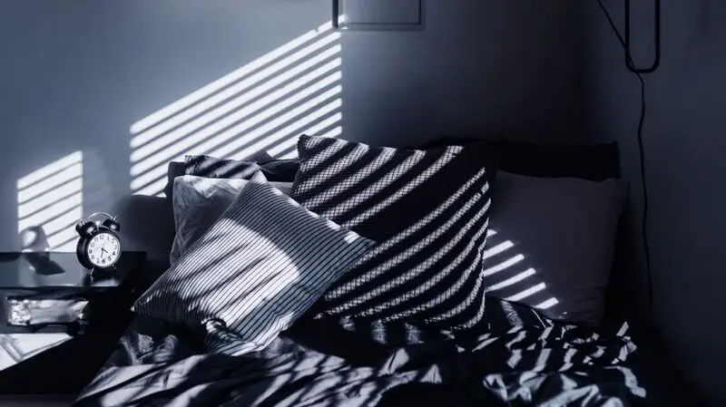 An alarm clock on a table next to a bed with pillows