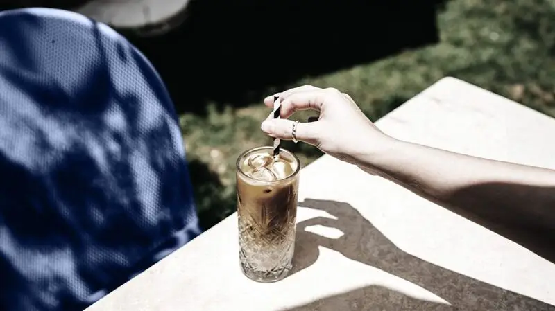A person holds the straw in a glass of iced coffee getting ready to stir it