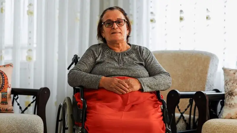 An older woman sits in a wheelchair with a blanket on her lap
