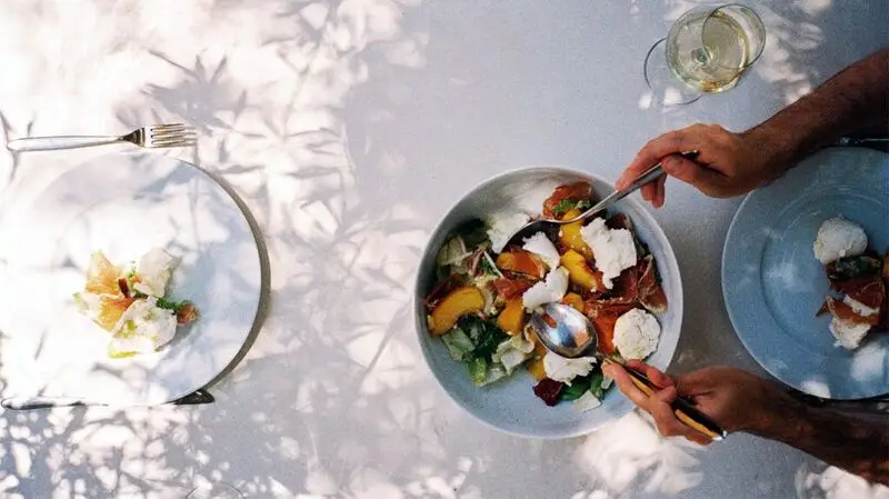 A person helping themselves to a bowl of Mediterranena-inspired salad with peaches, feta cheese, and greens