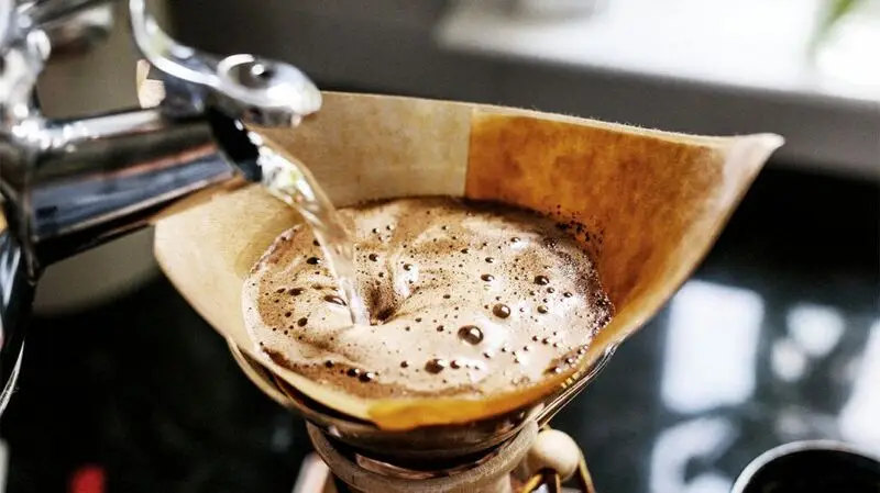 A person brewing drip coffee by pouring hit water over a paper filter