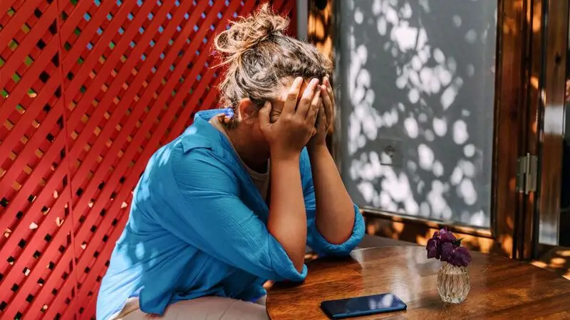 A woman sitting at an outdoor table covers her face