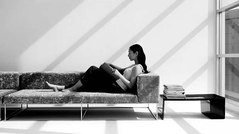 A woman sitting on a sofa with her legs stretched out, reading a book