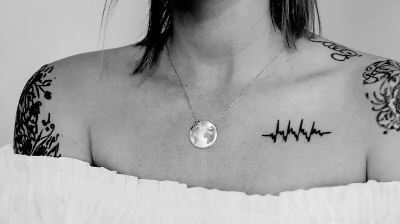 A close up image of a woman's collar bone featuring a tattoo depicting a heartbeat pulse line
