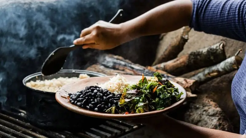 A woman out of frame puts a scoop of rice on a plate full of navy beans and salad