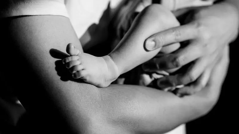 black and white photo zooming in on parent's arms cradling a baby