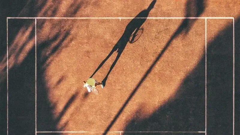 A drone view of a person on a tennis court outside under the sun