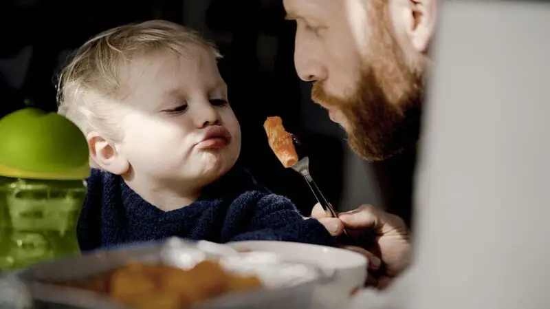 A father feeds a piece of pasta to his young son