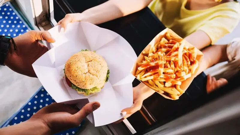 A food server hands a hamburger and some fries to a customer