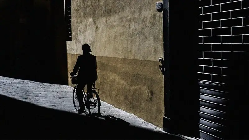 Silhouette of person riding a bike on a sidewalk