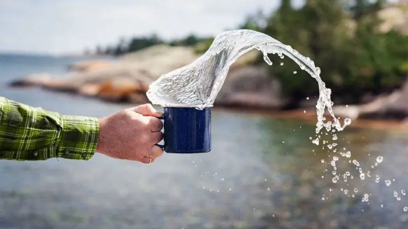 A person rinses a mug with water at a lake