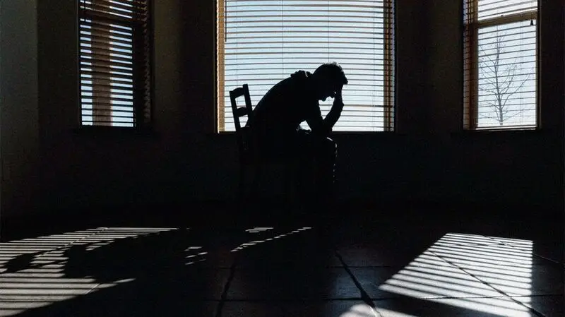 A man holds his head in his hands as he sits on a bed