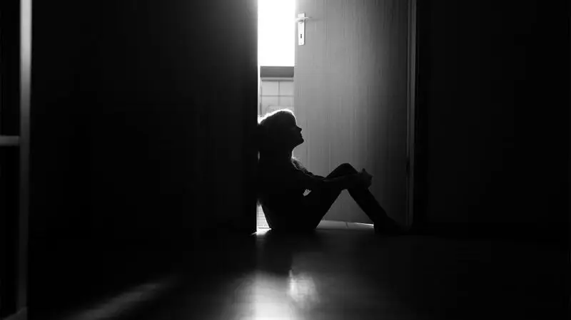 The silhouette of child sitting in a doorway of a dark hall