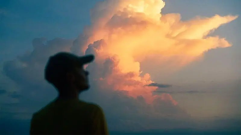 A man gazes at orange-tinted clouds in the sky