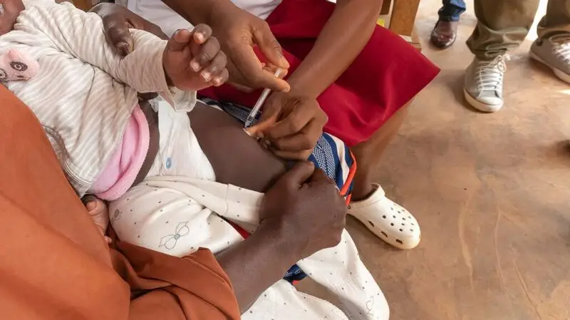 close-up of Black parent holding their small child as they receive the malaria vaccine