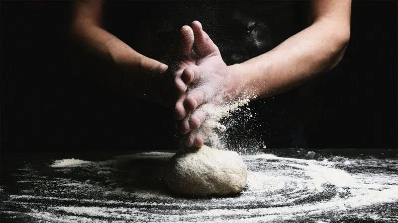 A close up of a person's hand while they are making bread with flour and kneading dough