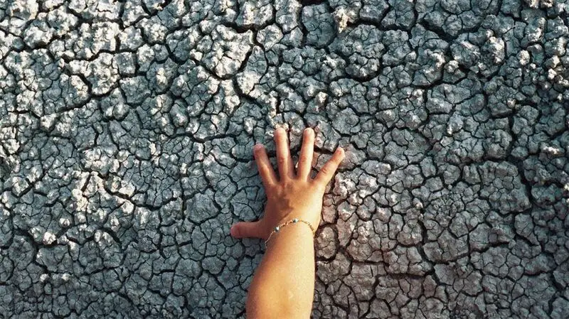A hand presses against some dry, cracked ground