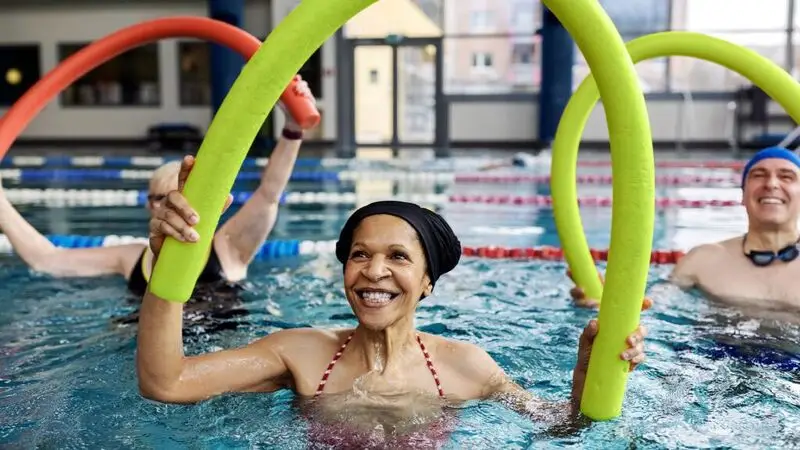 An older woman uses a styrofoam noodle during a workout in a swimming pool