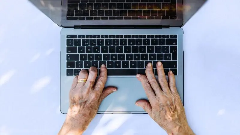 An older person's wrinkled hands on a computer keyboard