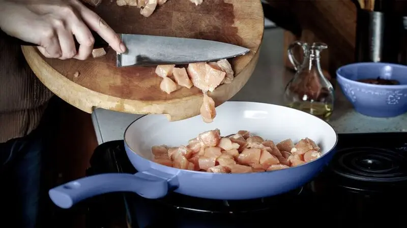 A person cooking diced chcicken breast in a pan, which is a good source of vitamin B