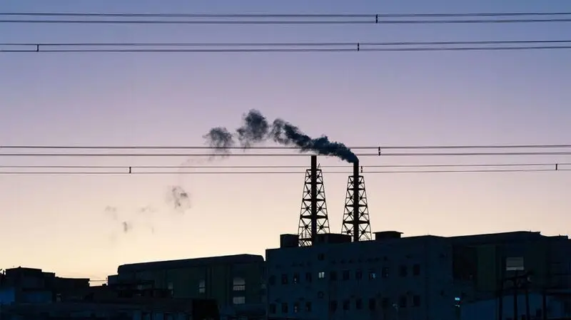 Dark smoke rises from an industrial chimney