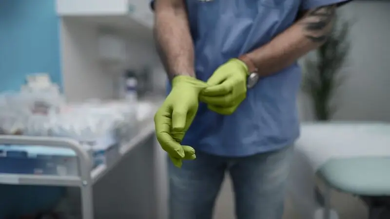 A surgeon puts on light green latex gloves