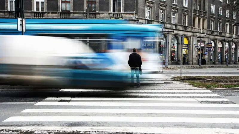 Person crosses the street near a blurred blue bus