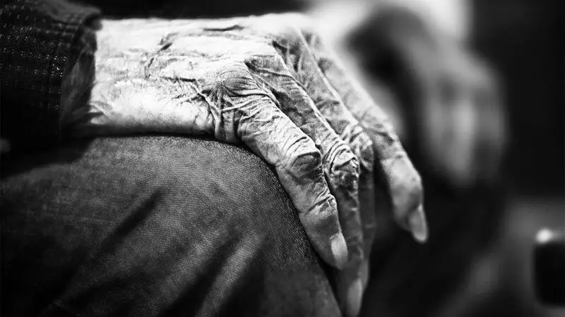 A close up of an old person's hands resting on their knee.