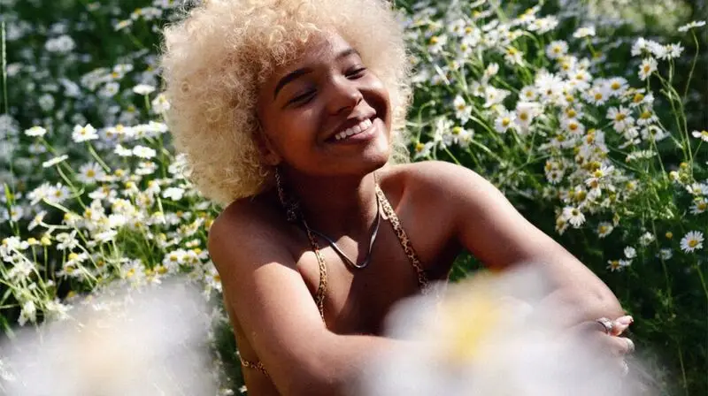 A woman hugging her knees and smiling in the sunshine.