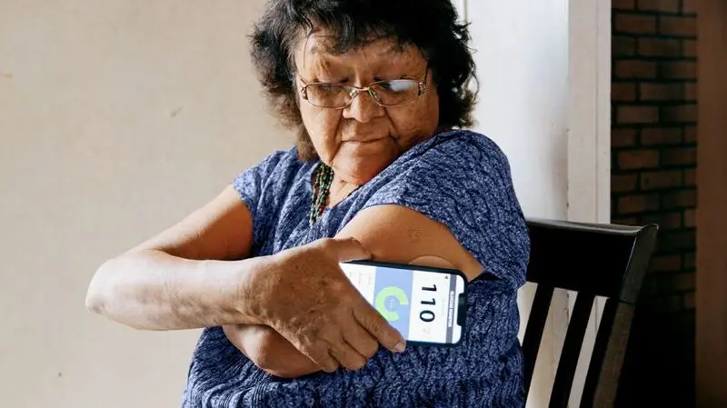 An older woman uses a blood glucose monitor at home
