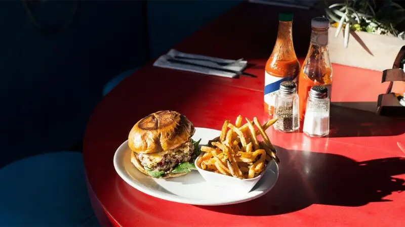 A plate of chips and a burger on a table with bottles of condiments on the side. 