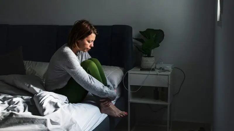 A woman meditates while sitting on the edge of a bed