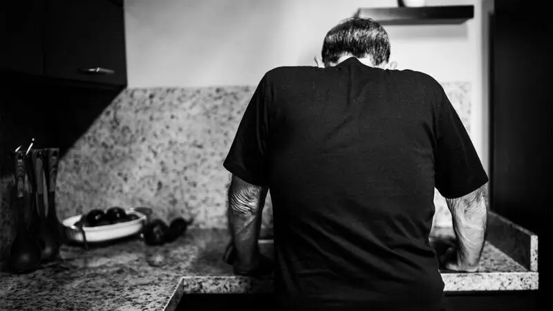 A man in a kitchen braces himself on a sink