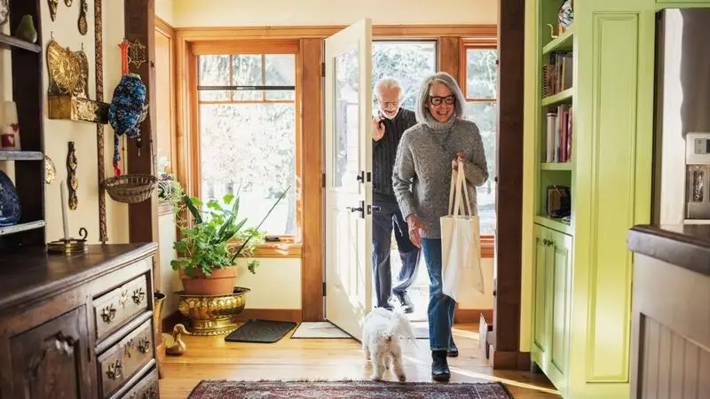 happy older couple greeted by a white dog at home