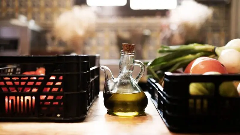 A glass container of olive oil sits on a kitchen counter