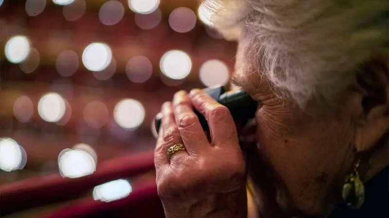 Older female looks through binoculars at the opera