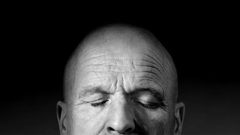 An older bald man closes his eyes