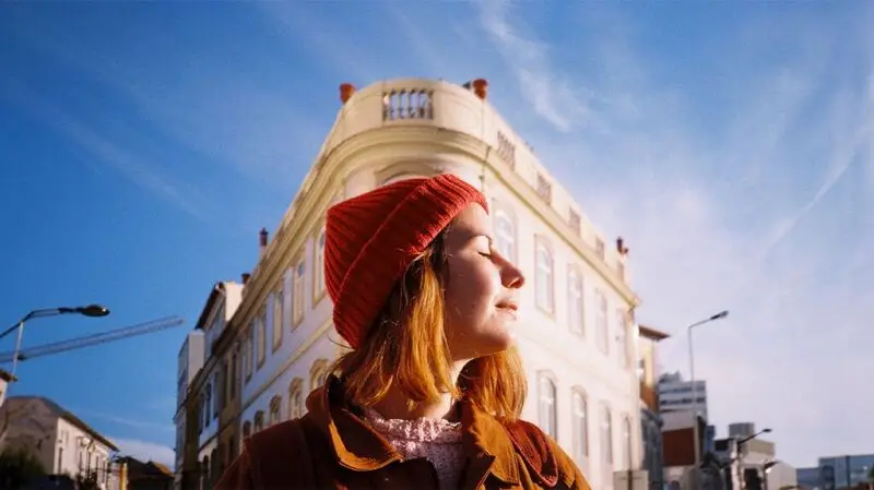 A woman stands in the sunshine with her eyes closed outside a building