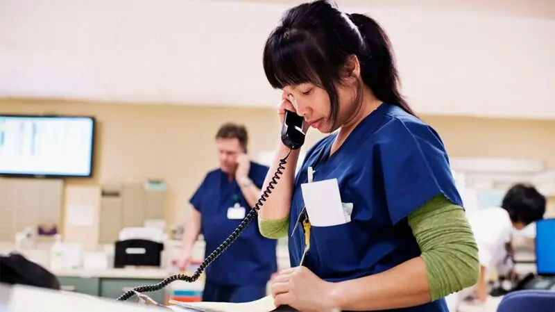 A nurse checking her notes while talking on the phone in a breast cancer ward