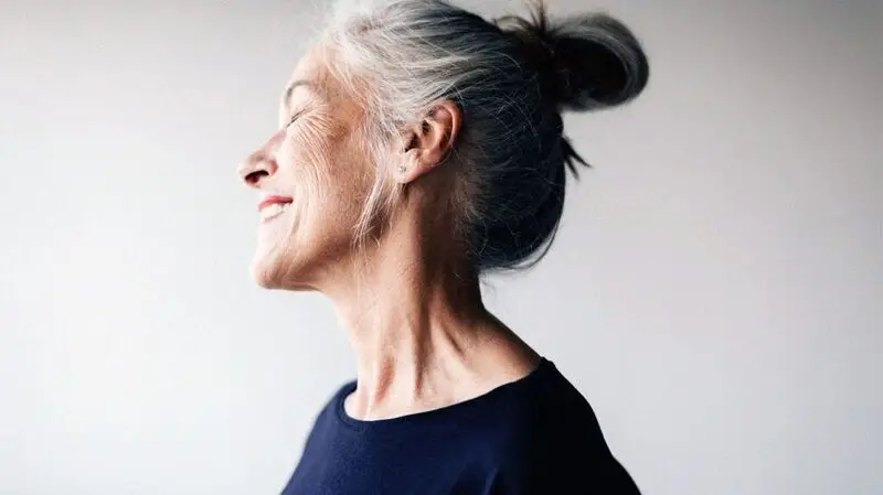 The side profile of an older adult woman smiling with her eyes closed