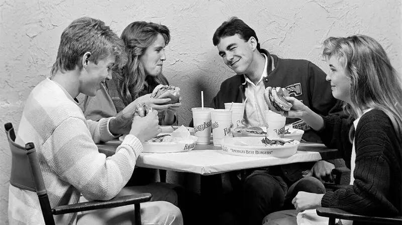 black and white photo of two white young women and two white young men eating burgers ay a fast-food table