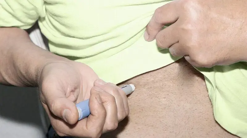 A person injecting themselves with a pen filled with medication for a chronic condition