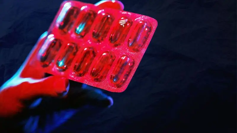 A person holding a blister pack of pills under ultraviolet lighting