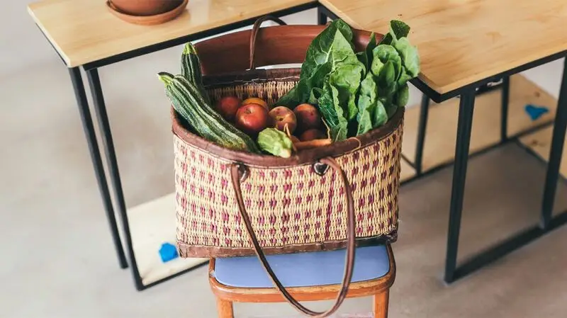 A woven bag full of fruits and vegetables on a chair