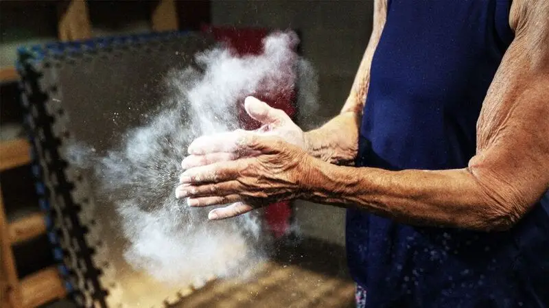 A close-up of an older adult in workout clothes rubbing their hands together as a cloud of chalk forms around 