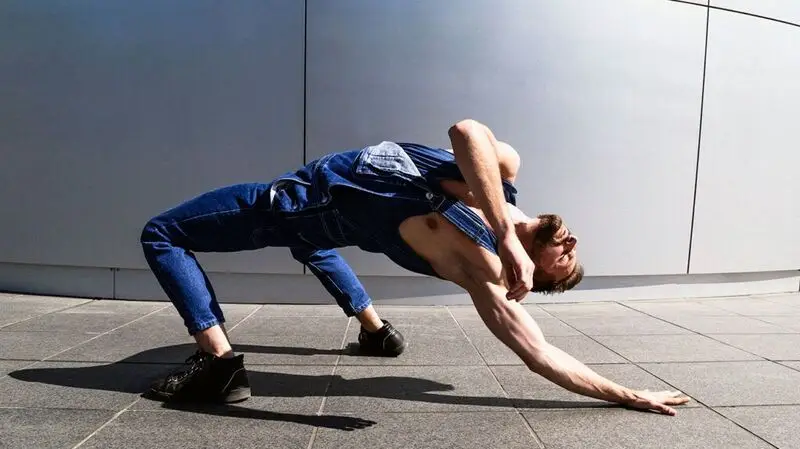 A man stretching his arm in a bridge pose as part of a modern dance performance outside