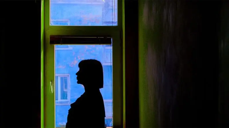 The side profile silhouette of a woman in front of a window at night