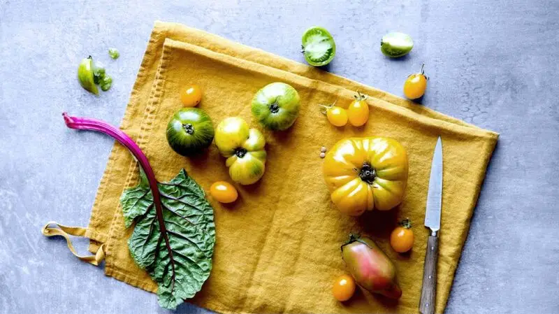 Fresh produce and vegetables such as kale and tomatoes on a kitchen cloth next to a cutting knife