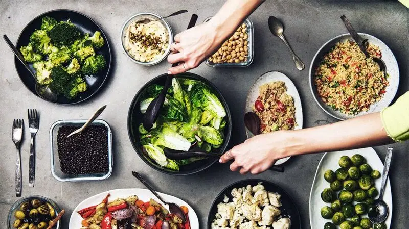 Various healthy Mediterranean-inspired dishes in plates on a table and a person mixing a bowl of fresh salad